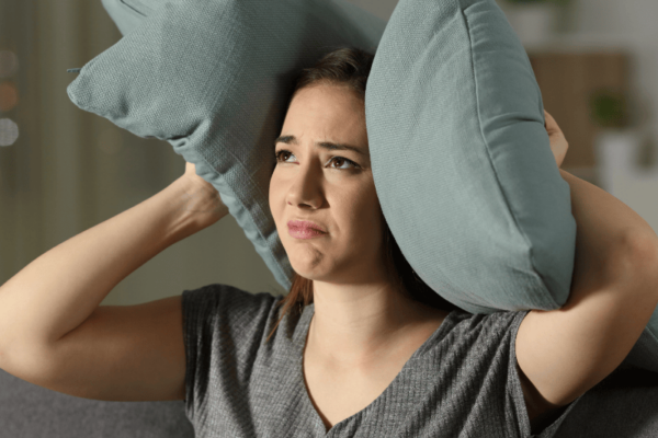 Foto van jonge vrouw die kussens op haar oren houdt omdat ze veel geluidsoverlast ervaart.